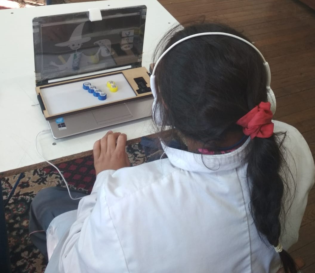 A girl with low vision sitting on a chair while playing with the blocks to solve the additive composition tasks by using the system iCETA. The iCETA setup is located on the table.